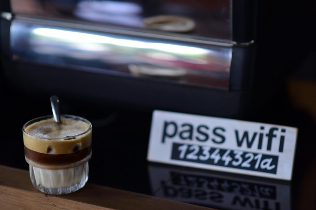 Glass of layered espresso coffee in a cafe with visible WiFi password sign, cozy atmosphere.